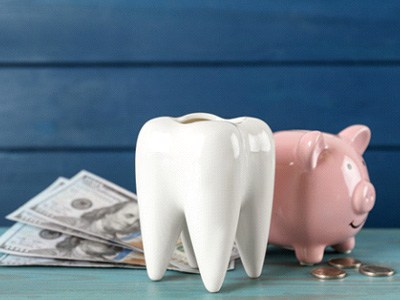 Dollar bills and coins next to a large ceramic tooth and a piggy bank