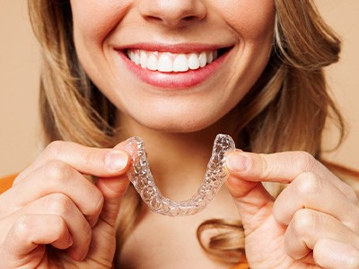 A woman holding a clear Invisalign tray with both hands