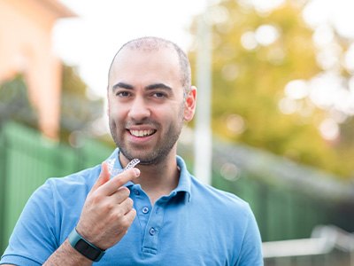 A man with a warm smile holding an Invisalign tray in his hand