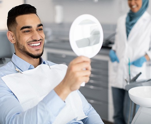 A handsome man admiring his new veneers in a hand mirror