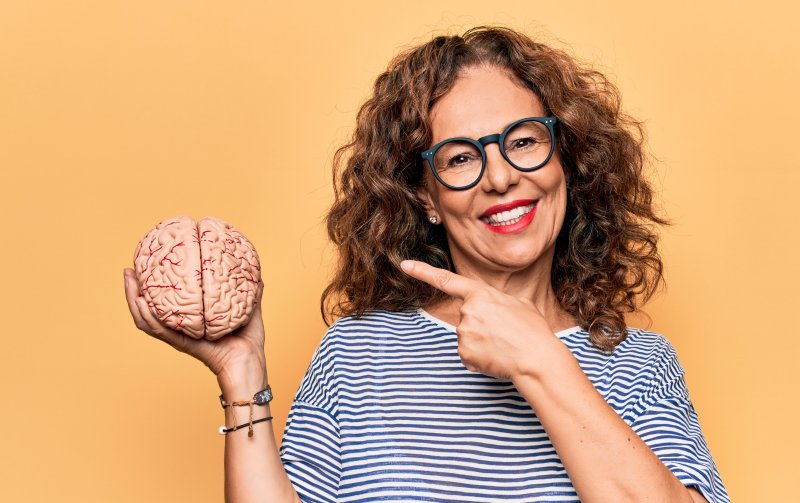 A smiling middle-aged woman pointing to a fake brain in her hand