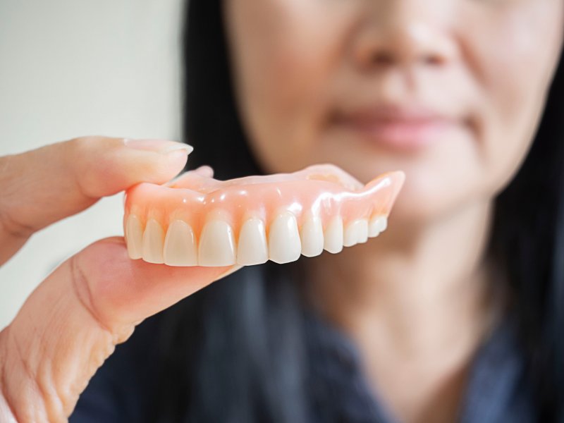 A woman holding a full denture between her fingers