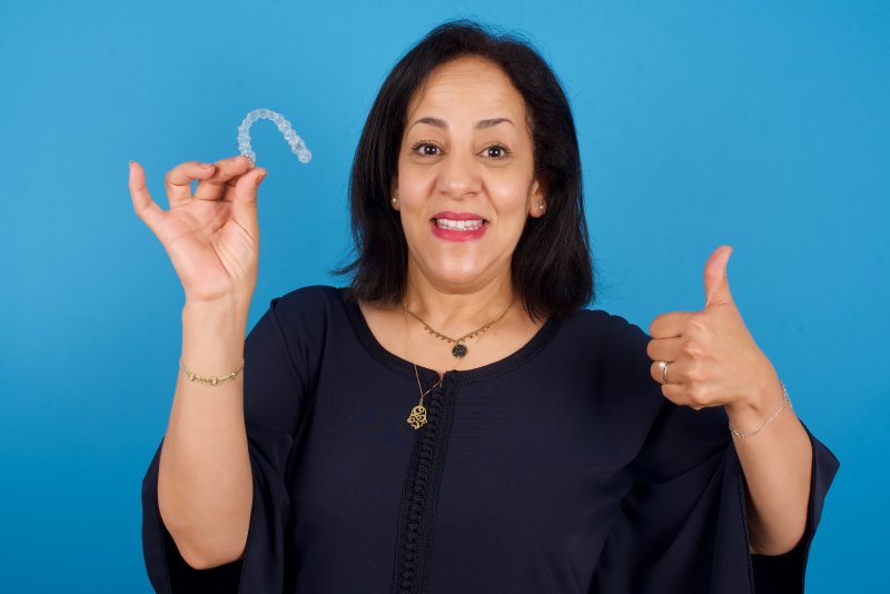 An older woman holding an Invisalign tray and giving a thumbs-up