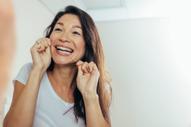 A woman flossing between her teeth in front of a mirror